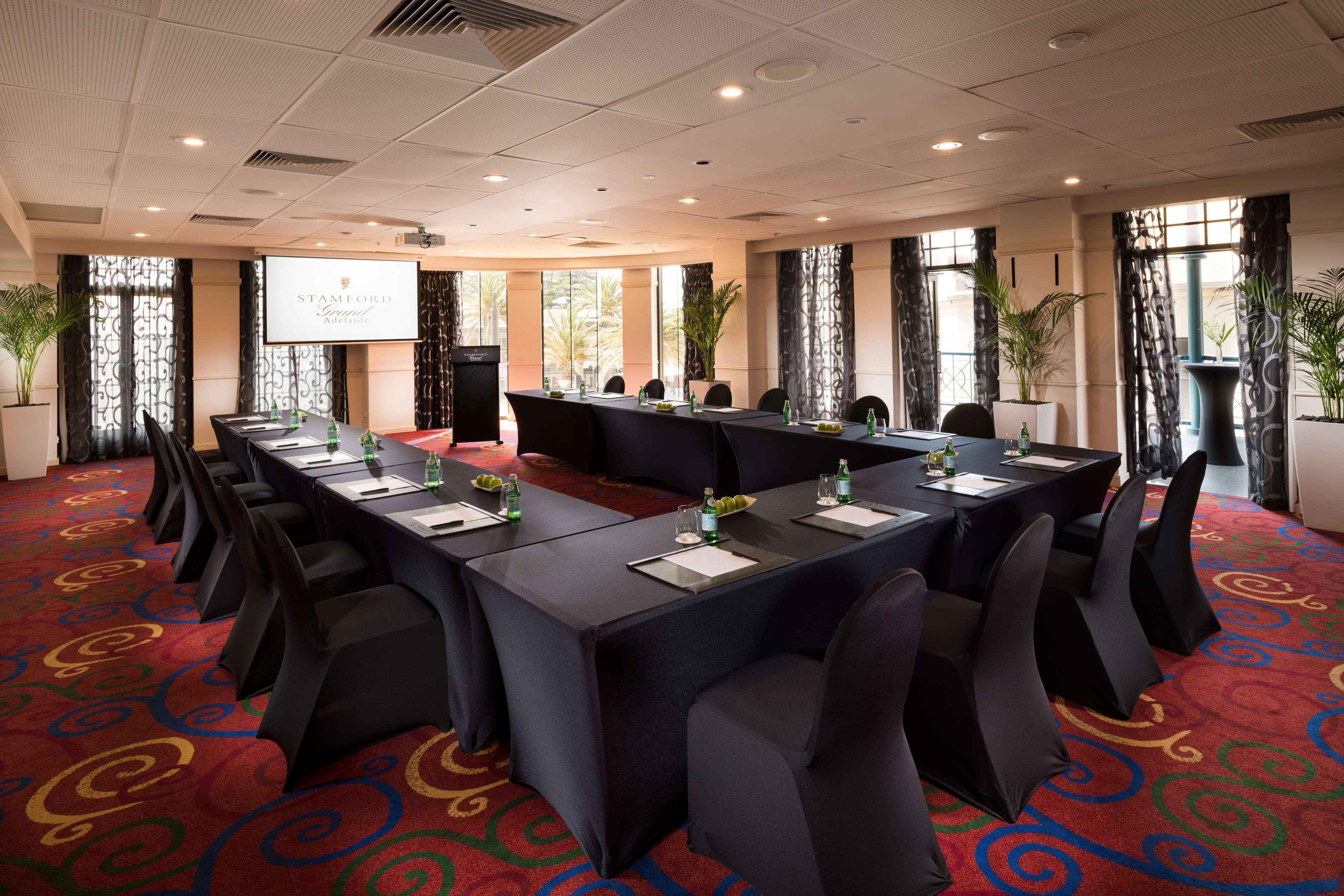 Stamford Grand Adelaide Hotell Glenelg Exteriör bild The photo shows a conference room set up for a meeting or presentation. There are several tables arranged in a U-shape, covered with black tablecloths. Each table has a notepad and a small bottle of water on it. The chairs around the tables are also 